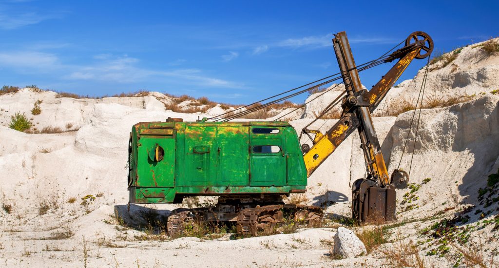 Limestone quarry with sparse vegetation and old abandoned and rusty excavator